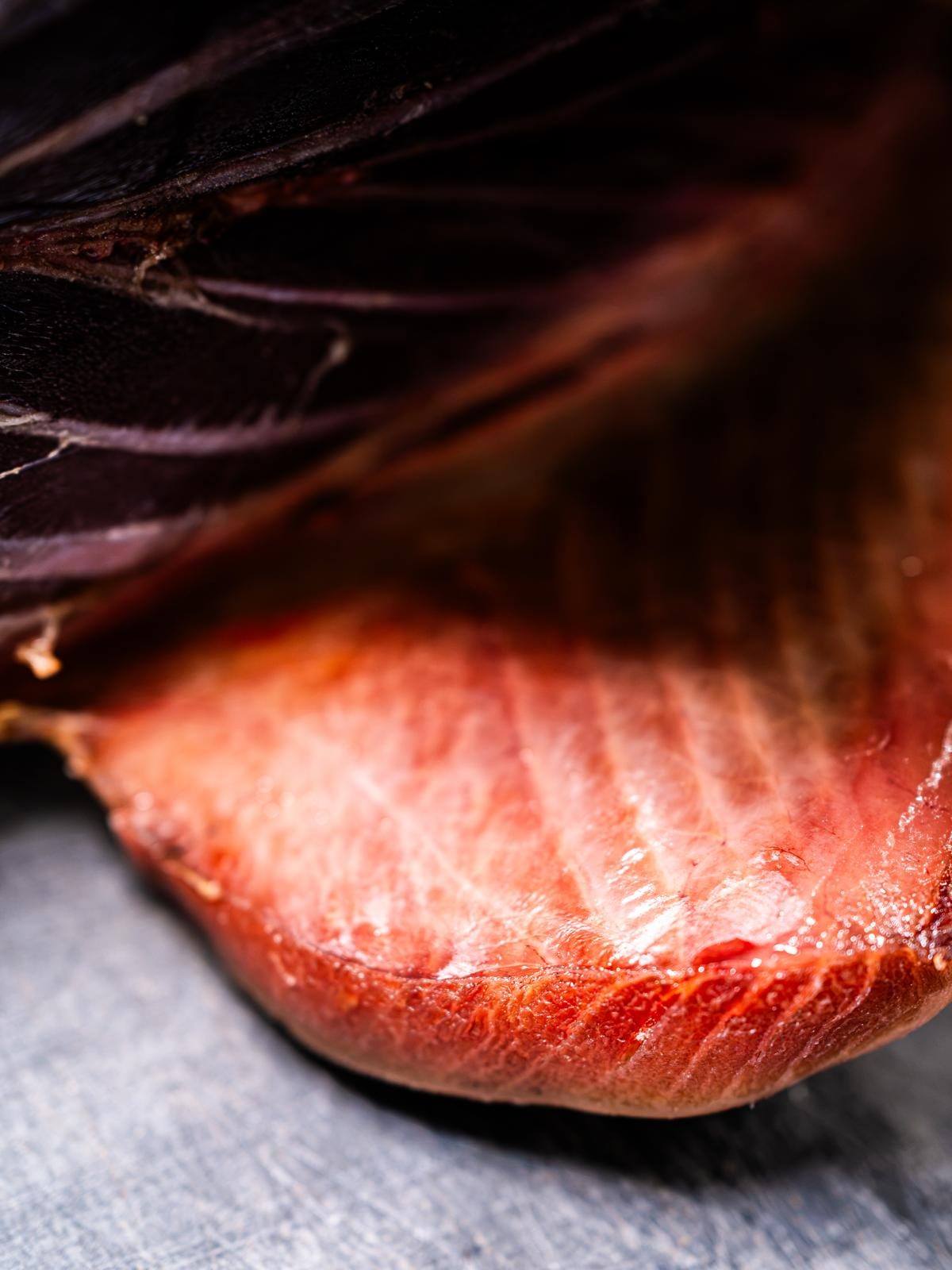 Un taglio di tonno da vicino: la carne rosata, venata di bianco, sotto la pelle scura.